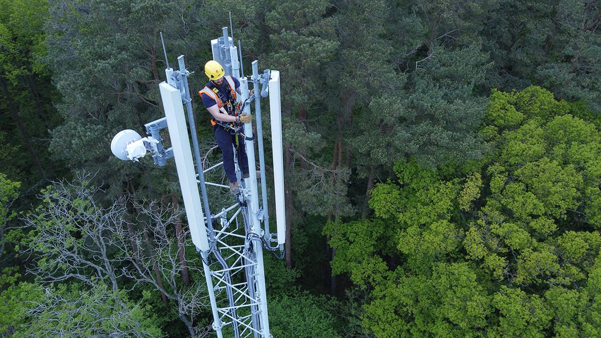 Mitie employee at the top of a telecoms mast, with green treetops below