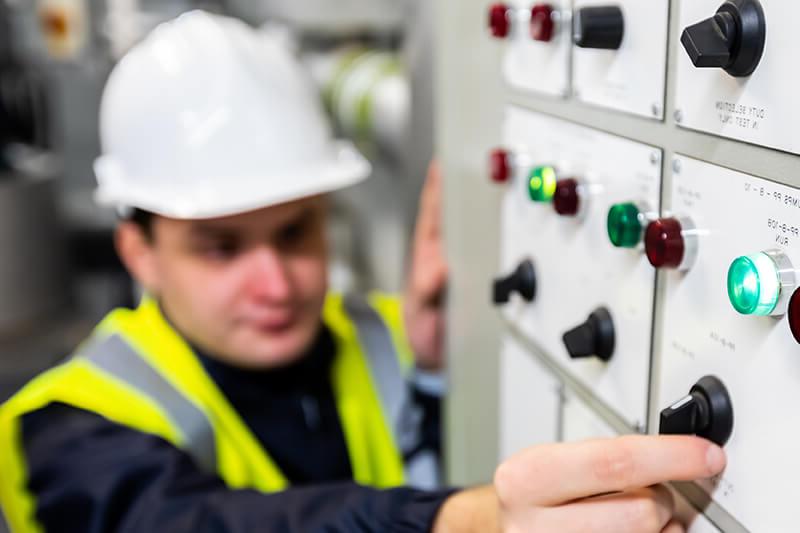 Engineer in high-vis vest and hard hat twists a dial on a large machine